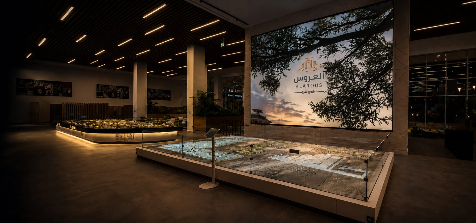 Spacious room with architectural scale models and digital screen showing text on an evening sky backdrop.