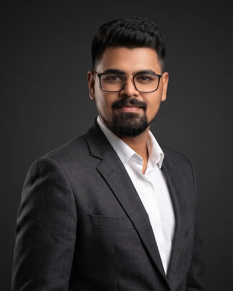Man with glasses and beard in dark suit and white shirt poses against a dark background.